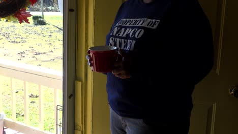 Hands-Only--African-American-Woman-looking-out-front-door-with-a-red-mug-of-coffee