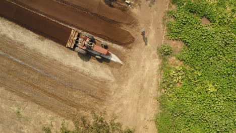 Tractor-amending-the-soil-in-the-farm-field-at-the-countryside,-cinematic-drone-shot