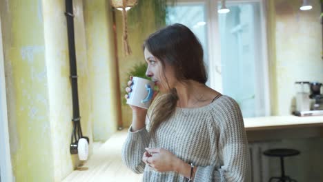 Young-european-Female-Student-is-enjoying-her-coffee-or-tea-at-the-coffeehouse-with-natural-background