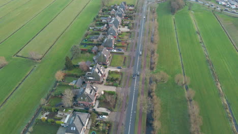 Aerial-of-cars-driving-over-a-calm-road-lying-next-to-a-row-of-standalone-houses-in-a-rural-area