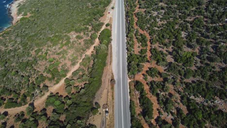 Road-in-the-mountains-of-Crete-with-cars-drivings-and-the-sea-with-green-forests-surrounding-the-road