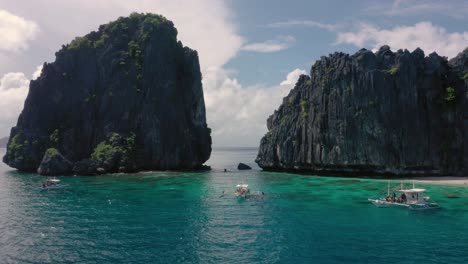 Aerial-of-limestone-cliffs,-turquoise-water-and-natural-archipelago-with-drone-flying-through-rocks-and-small-boats-in-El-Nido,-Palawan,-Philippines