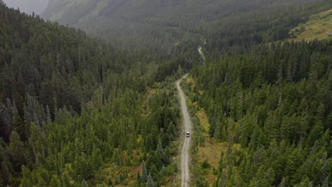 Wide-aerial-view-of-SUV-driving-mountain-forest-road-in-British-Columbia