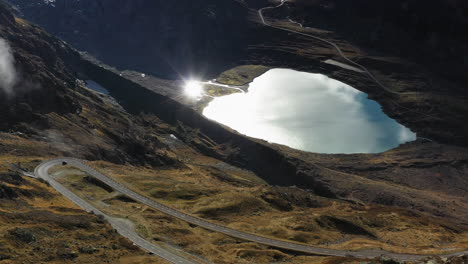 Cinematic-aerial-shot-of-the-Steinsee-Lake-along-the-Susten-Pass,-Switzerland,-with-a-sun-flare