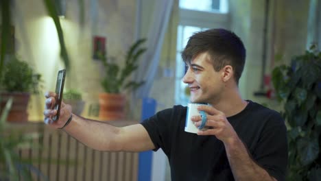 Junger-Europäischer-Männlicher-Student-Macht-Selfie-Und-Genießt-Seinen-Kaffee-Oder-Tee-Im-Kaffeehaus-Mit-Natürlichem-Hintergrund