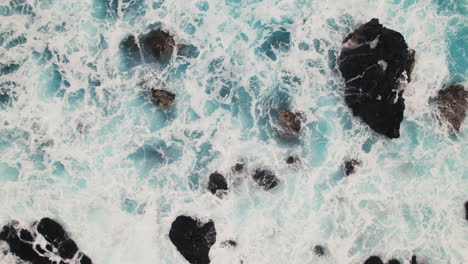 Top-down-view-of-waves-crashing-on-rocky-beach-in-Hawaii---aerial-pan-left-to-right
