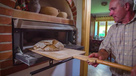 Old-baker-man-taking-fresh-delicious-bread-from-old-fashioned-oven,-Medium-shot