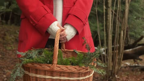 Woman-in-red-coat-showing-a-basket-full-of-evergreen-branches-for-wreath-making-holiday-season-diy-4k-slow-motion