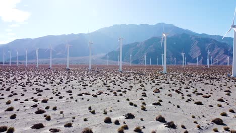 Majestic-wind-turbines-farm-in-desert-area-with-mountain-range-in-background,-aerial-drone-view