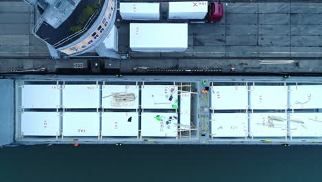 Descending-top-down-shot-worker-on-container-ship-in-harbor