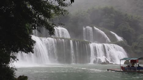 Tourist-raft-getting-close-to-Ban-Gioc-waterfall,-the-largest-transborder-waterfall-in-Vietnam-and-China-during-a-rainy-day