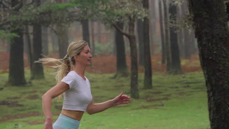 Fit-attractive-blond-woman-running-through-misty-forest-in-slow-motion