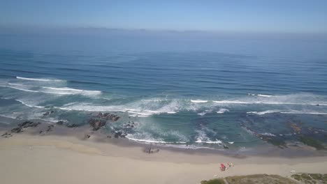 Aerial-view-of-drone-flying-above-beautiful-beach-with-views-of-ocean-waves-and-water-crashing-on-to-sandy-beach-from-top-angle