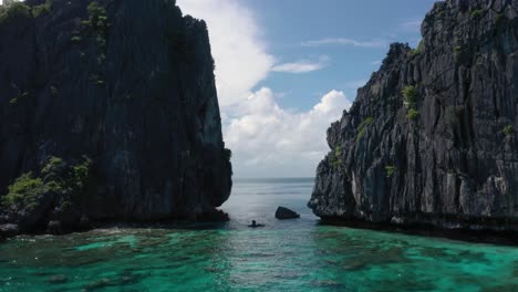 Aerial-drone-flying-through-huge-limestone-cliffs,-turquoise-water-and-natural-archipelago-with-rocks-and-small-boats-in-El-Nido,-Palawan,-Philippines