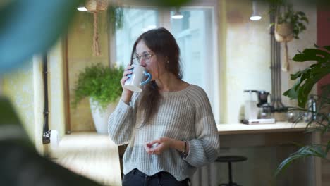 Young-european-Female-Student-is-drinking-her-coffee-or-tea-at-the-coffeehouse-with-natural-background