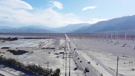 Busy-freeway-and-massive-desert-wind-turbine-farm,-aerial-drone-view