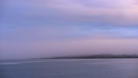 Nebel-über-Meer-Und-Küstenstadt-Bei-Sonnenaufgang-Mit-Ruhigem-Wasser-Und-Buntem-Himmel