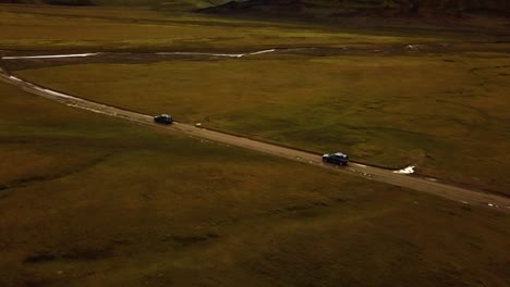Aerial-view-over-two-cars-speeding-on-a-dirt-road-through-icelandic-highlands