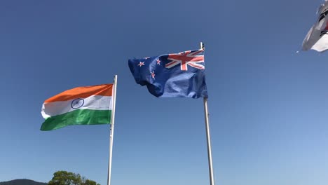 Die-Nationalflaggen-Von-Indien-Und-Neuseeland-Flattern-Im-Wind-Unter-Einem-Klaren-Blauen-Himmel,-Wobei-Ein-Teil-Der-Koreanischen-Flagge-In-Der-Linken-Oberen-Ecke-Weht