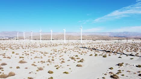 Line-of-white-green-energy-wind-turbines-spinning-in-deadly-desert,-aerial-descend-view