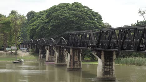 A-static-shot-of-the-iconic-railway-Bridge-Over-the-River-Kwai,-the-calm-waters-of-the-Khwae-Noi-river-flows-below-in-Kanchanaburi,-Thailand