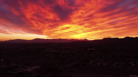 Aerial-view-of-a-Fire-Sunset-over-the-Estrella-Mountains-and-South-Mountain-near-Tempe-Arizona,-Red-yellow-orange-clouds