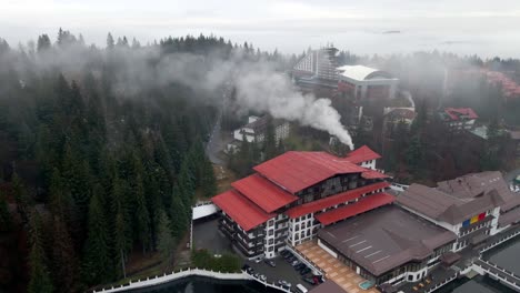Smoke-Rises-From-The-Chimney-Of-A-Building-Near-The-Dense-Forest-In-Poiana-Brasov,-Romania