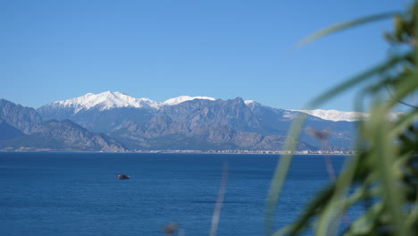 Turkish-boat-crossing-the-Mediterranean-Sea-with-green-foliage-and-snow-covered-mountains-visible