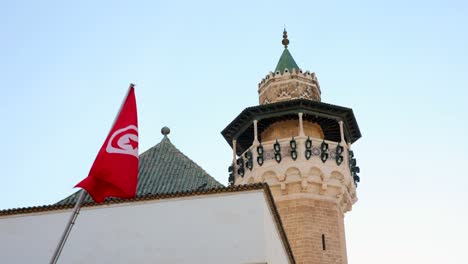Tiefwinkelansicht-Einer-Tunesien-Flagge-Mit-Der-Fassade-Eines-Turms-Und-Einer-Mauer-Als-Hintergrund