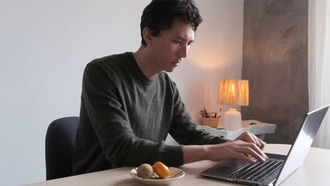 Hombre-Asiático-Mixto-Escribiendo-En-Su-Computadora-Portátil-Mientras-Trabaja-Desde-Casa