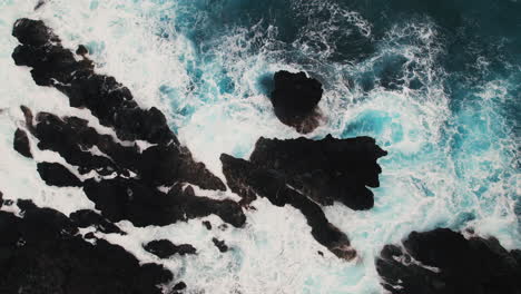 Top-down-aerial-shot-of-white-water-crashing-around-dark-lava-rocks-in-Hawaii