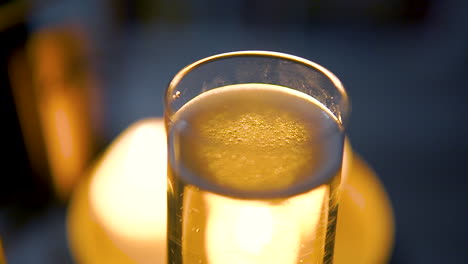 Glassware-Filled-With-Bubbly-Champagne,-Blurred-Candlelights-In-Background