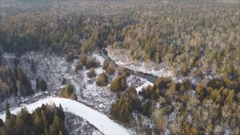 Drone-Shot-Of-Road-Surrounded-By-Coniferous-Forest-During-Winter,-Fresh-Snow-And-Creek