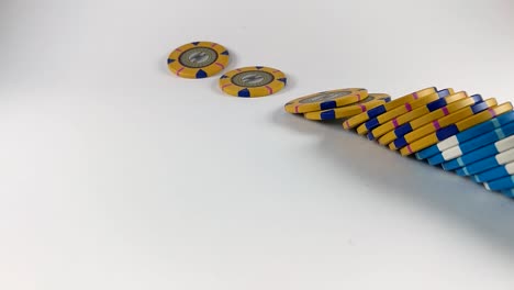 Stack-of-yellow-and-blue-poker-chips-falling-down-on-a-white-table,-SLOMO,-ISOLATED