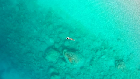 Top-down-Aerial-of-a-Girl-Floating-and-Lying-in-paradise-Turquoise-Ionian-Sea-in-Greece-Myrtos-Beach