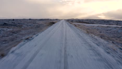 Toma-Aérea-Ascendente-De-Una-Carretera-Helada-Rodeada-De-Un-Campo-De-Lava-Cubierto-De-Nieve-En-Islandia
