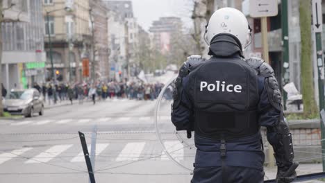 Unrecognizable-riot-police-officer-protecting-the-city---view-from-behind-back-of-cop,-blurred-background-demonstration