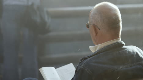 Close-up-shot-of-an-elderly-gentlemen-relaxing-reading-a-book-at-a-landmark-graduation-tower-in-Poland-with-salt-water-mist-passing-by