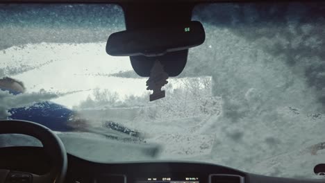 A-view-of-the-snowy-windshield-of-a-car,-from-which-a-man-is-clearing-snow