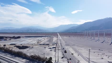 Endless-desert-highway-and-massive-wind-turbine-farm-on-sandy-desert-land,-aerial-drone-view
