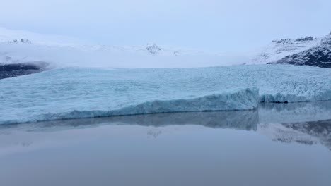 Luftaufnahme-Der-Gletscherlagune-Und-Der-Schneebedeckten-Berge-Im-Hintergrund---Moräne-Beeinflusste-Das-Schmelzen-Des-Eisgletschers---Globale-Erwärmung-Auf-Der-Erde