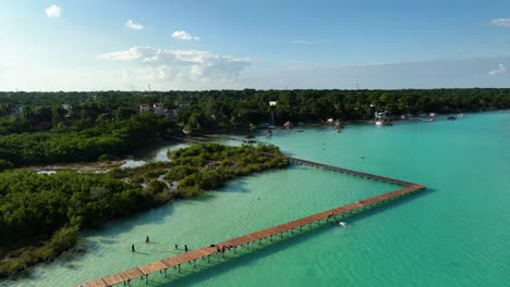 People-walking-on-the-piers-at-the-Area-natural-protegida-Parque-Laguna-de-Bacalar,-in-sunny-Mexico---Aerial-view