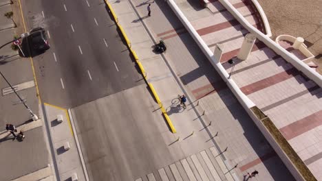 Aerial-tracking-shot-of-cyclist-riding-on-coastal-street-of-Mar-del-Plata-beside-beach-during-sunny-day