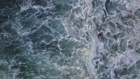 Aerial:-surfer-paddling-in-breaking-wave-whitewater,-bird's-eye-view