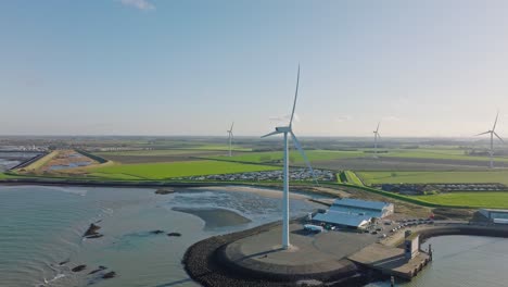 Aerial-slow-motion-shot-of-wind-turbines-in-a-rural,-coastal-area-in-the-Netherlands-against-a-blue-sky-around-sunset
