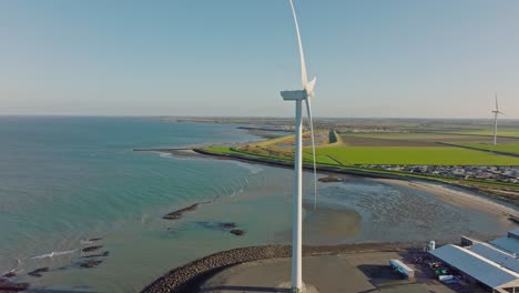 Aerial-slow-motion-shot-of-a-wind-turbine-along-the-coast-in-a-rural-area-in-the-Netherlands-against-a-blue-sky-on-a-sunny-day