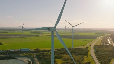 Aerial-slow-motion-shot-of-wind-turbines-and-a-road-in-a-rural-area-of-the-Netherlands-around-sunset-on-a-beautiful-sunny-day