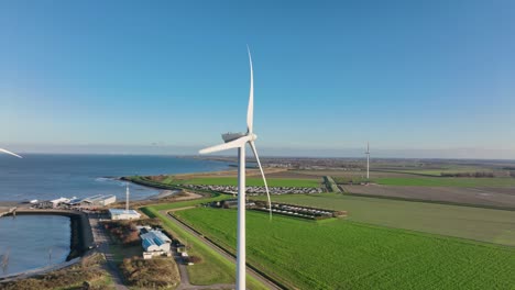 Aerial-slow-motion-shot-of-wind-turbines-in-a-rural-area-in-the-Netherlands-against-a-blue-sky-on-a-sunny-day