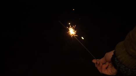 Woman's-Hand-Holding-Glittering-Fairy-Sparkler-Candle-Stick-On-New-Year's-Eve