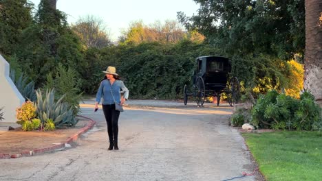 Hispanic-Female-walking-away-from-vintage-carriage-at-Rancho-Camulos-Museum,-sunny-afternoon